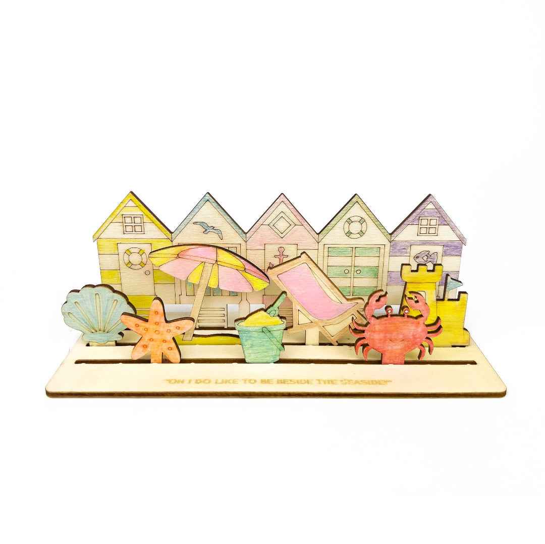Colourful beach-themed wooden model with houses, sandcastle, and beach accessories on a white background