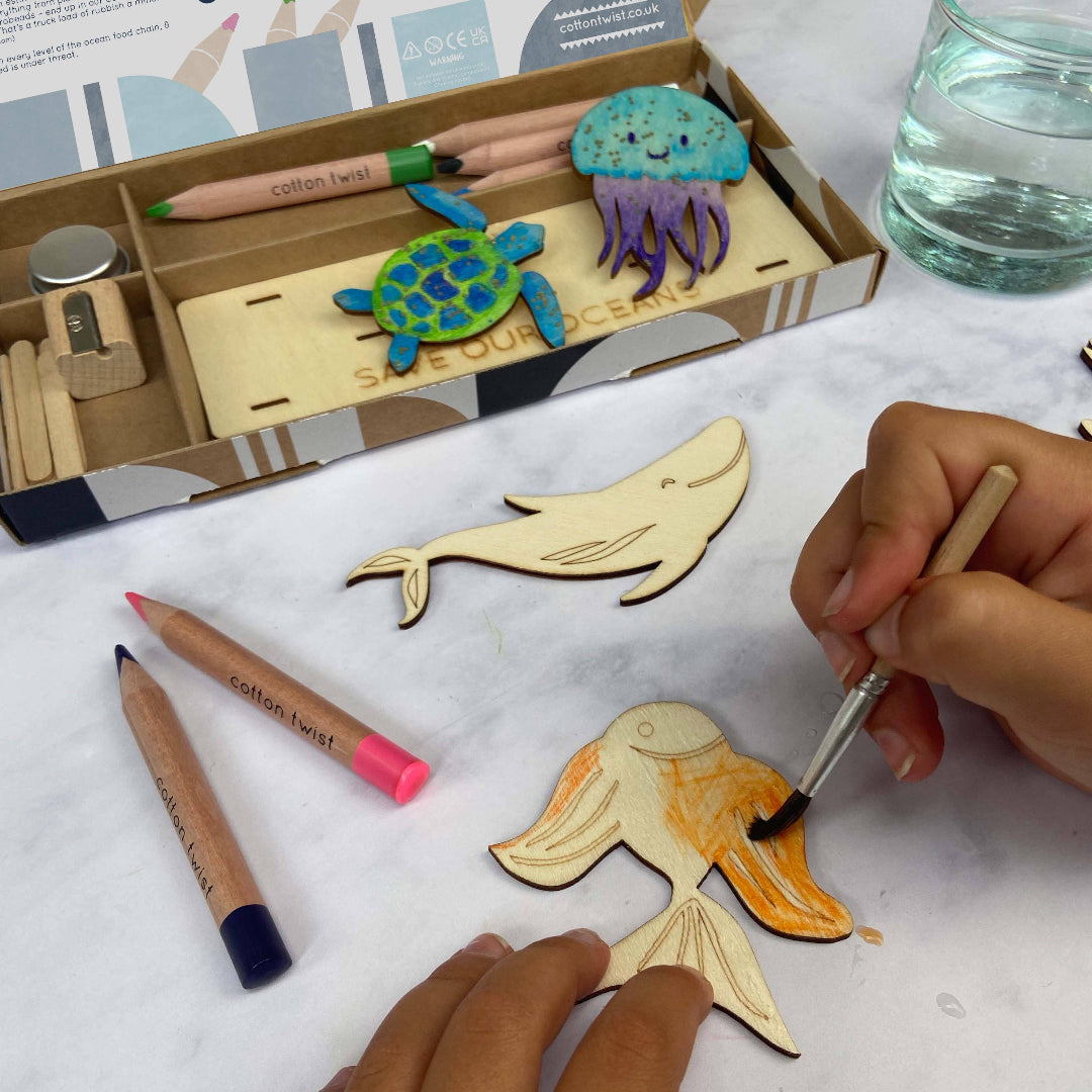 Person painting wooden animal shapes with markers and a paintbrush on a white surface.