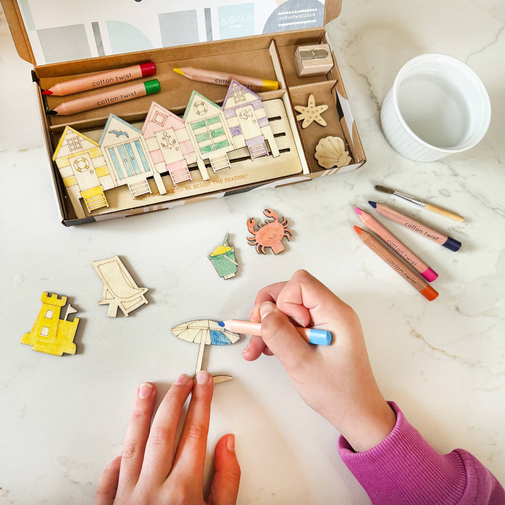 Children's craft activity with wooden houses and colorful markers on a marble surface.