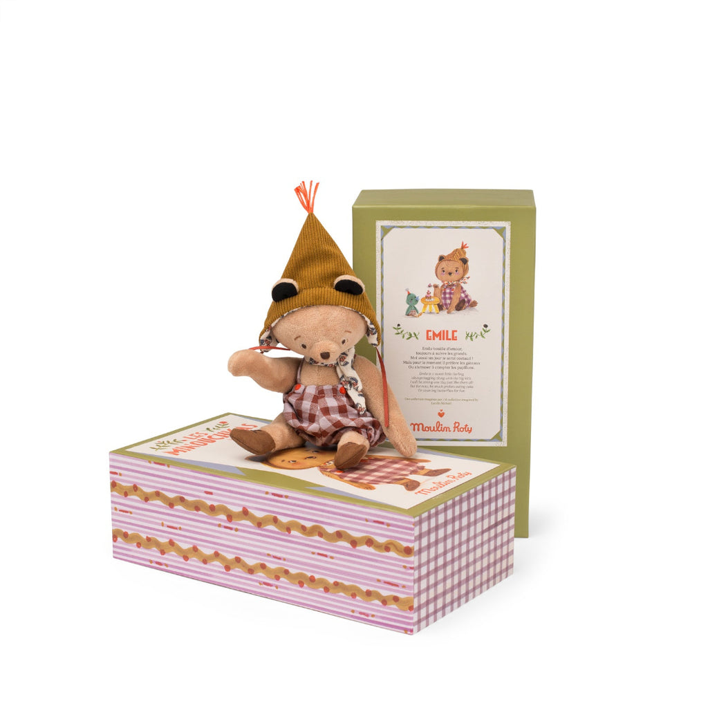 Small teddy bear in a checkered outfit with a hat, sitting on a decorative box with a card, on a white background.