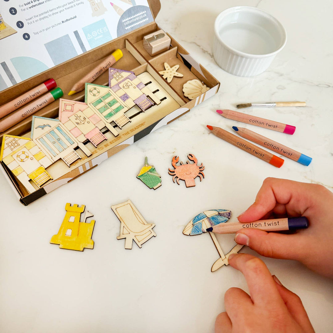 Wooden craft items and markers on a table with a hand holding a marker.
