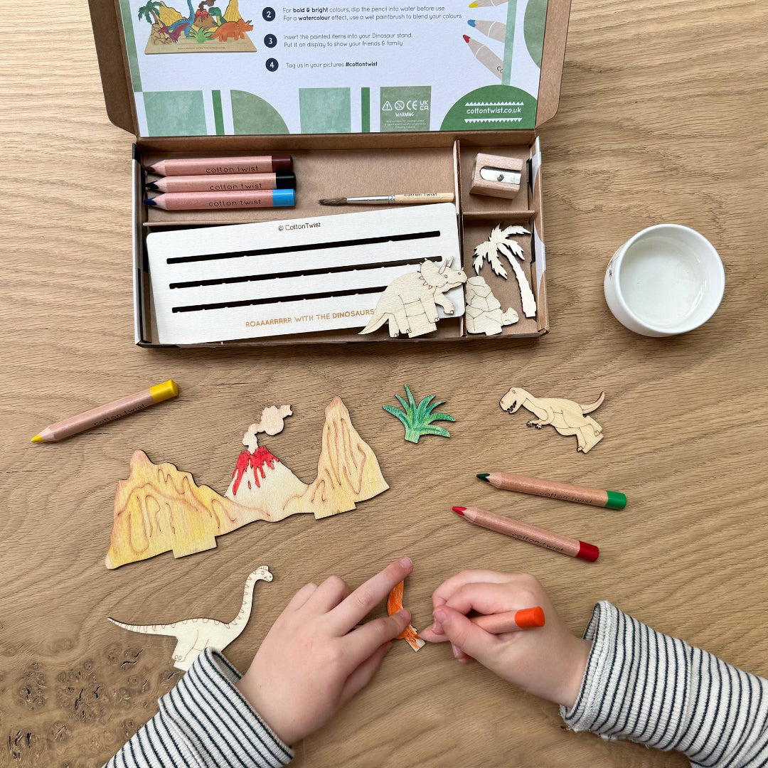 Children playing with a dinosaur-themed craft set on a wooden table.