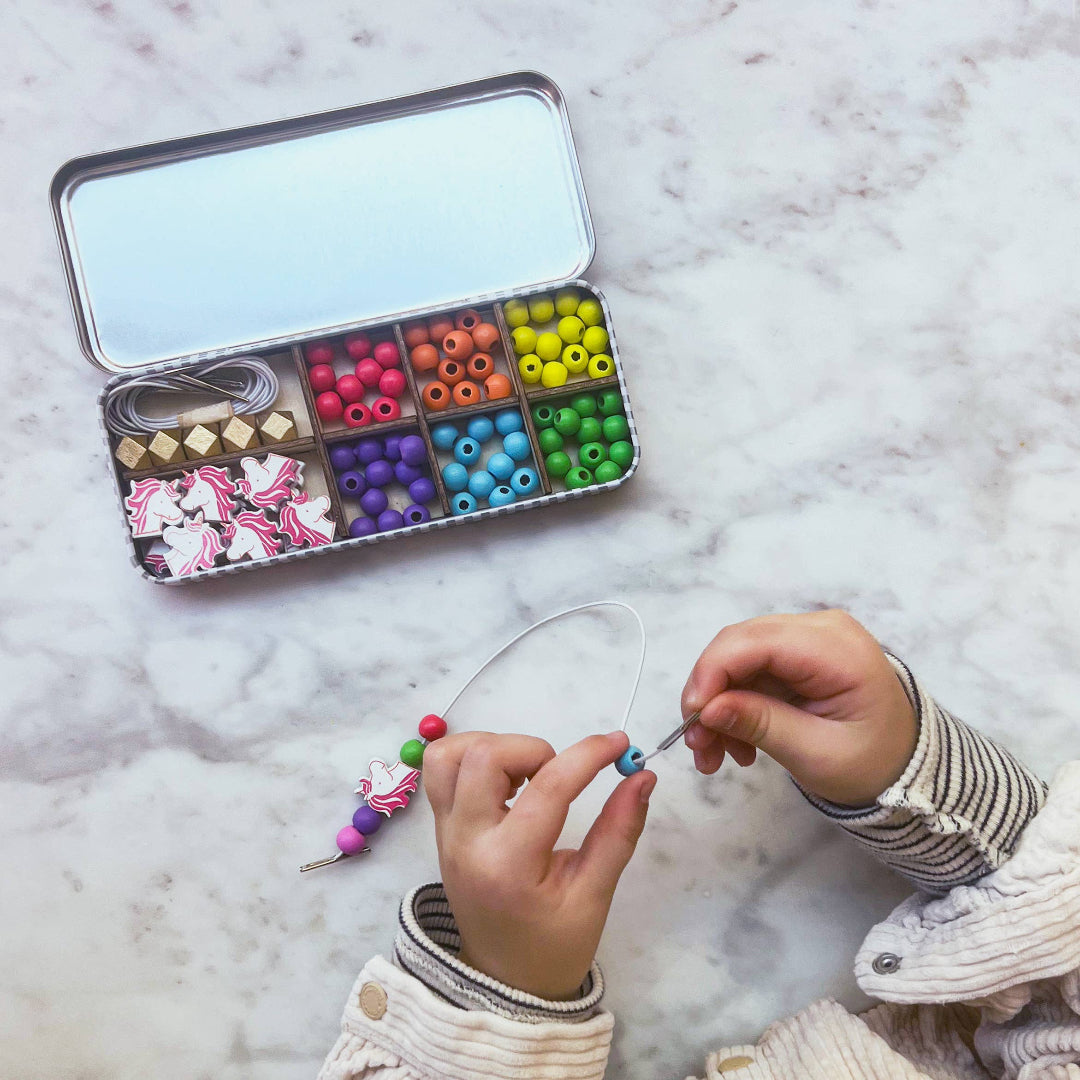 Colourful bead set in a tin with hands threading beads on a string on a marble surface