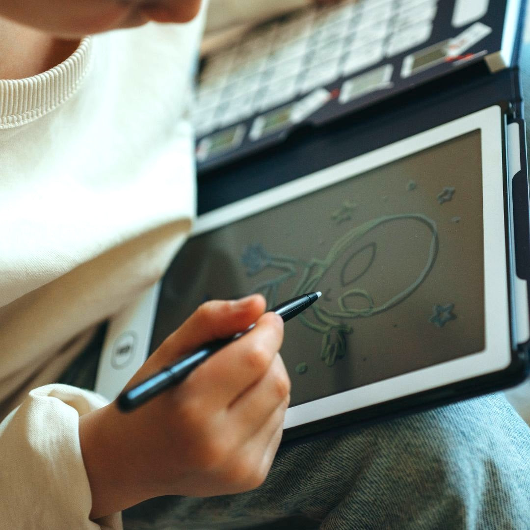 Child tracing an alien with stars on the KIDYDRAW MINI screen using the stylus, navy Galaxy card holder above
