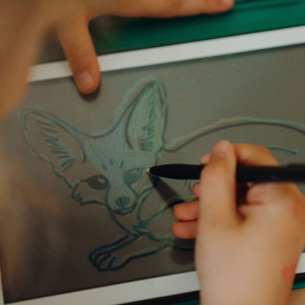 Close-up of a child tracing a fennec fox on the KIDYDRAW MINI screen with the stylus