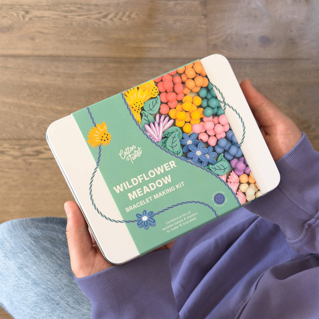 Hands holding the Wildflower Meadow Bracelet Making Kit tin over a lap in jeans