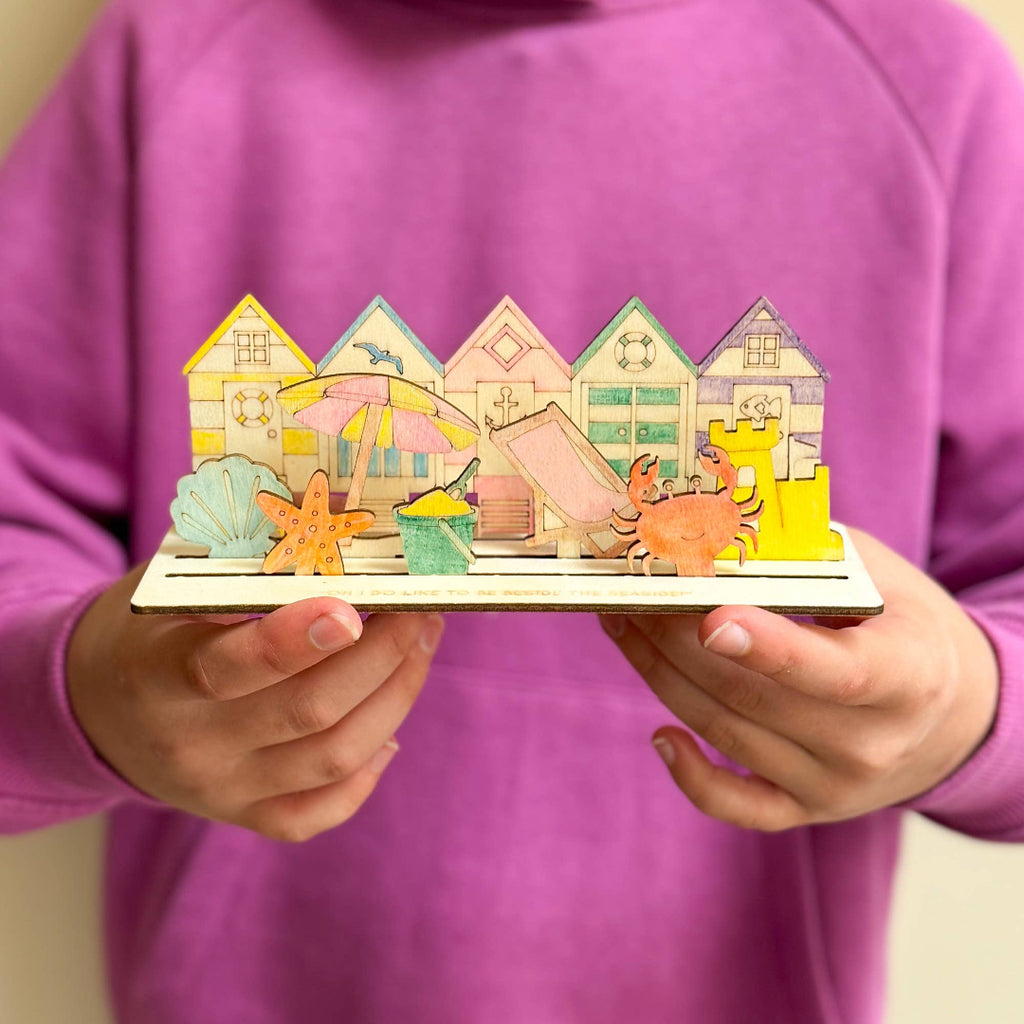 Child holding a colorful wooden toy with beach-themed houses and animals.