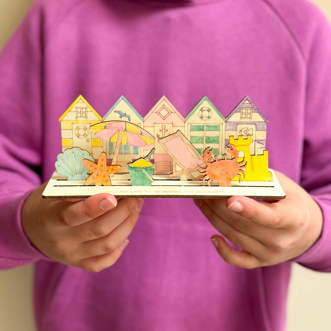 Child holding a colorful wooden toy with beach-themed houses and animals.