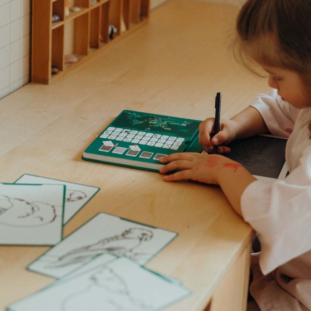 Little girl drawing on the KIDYDRAW MINI at a wooden desk with the green Animals card holder and refill cards beside her