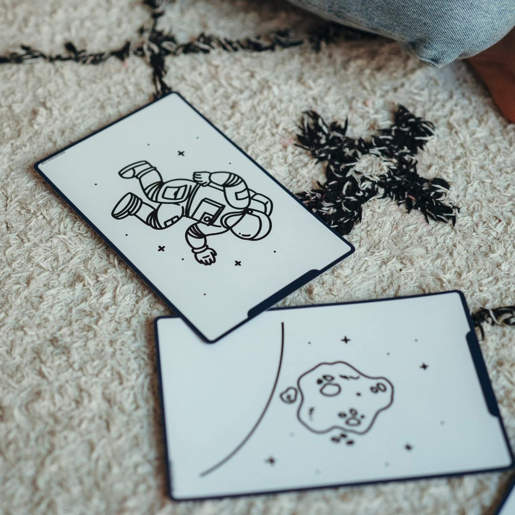 Galaxy refill cards with a floating astronaut and an asteroid drawing laid on a cream and black rug
