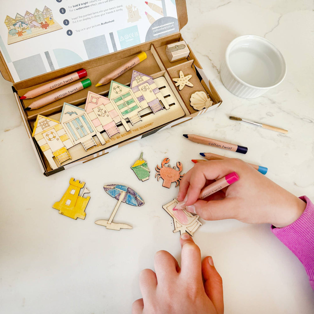 Colourful wooden house and beach-themed stamps on a table with a hand holding a stamp.