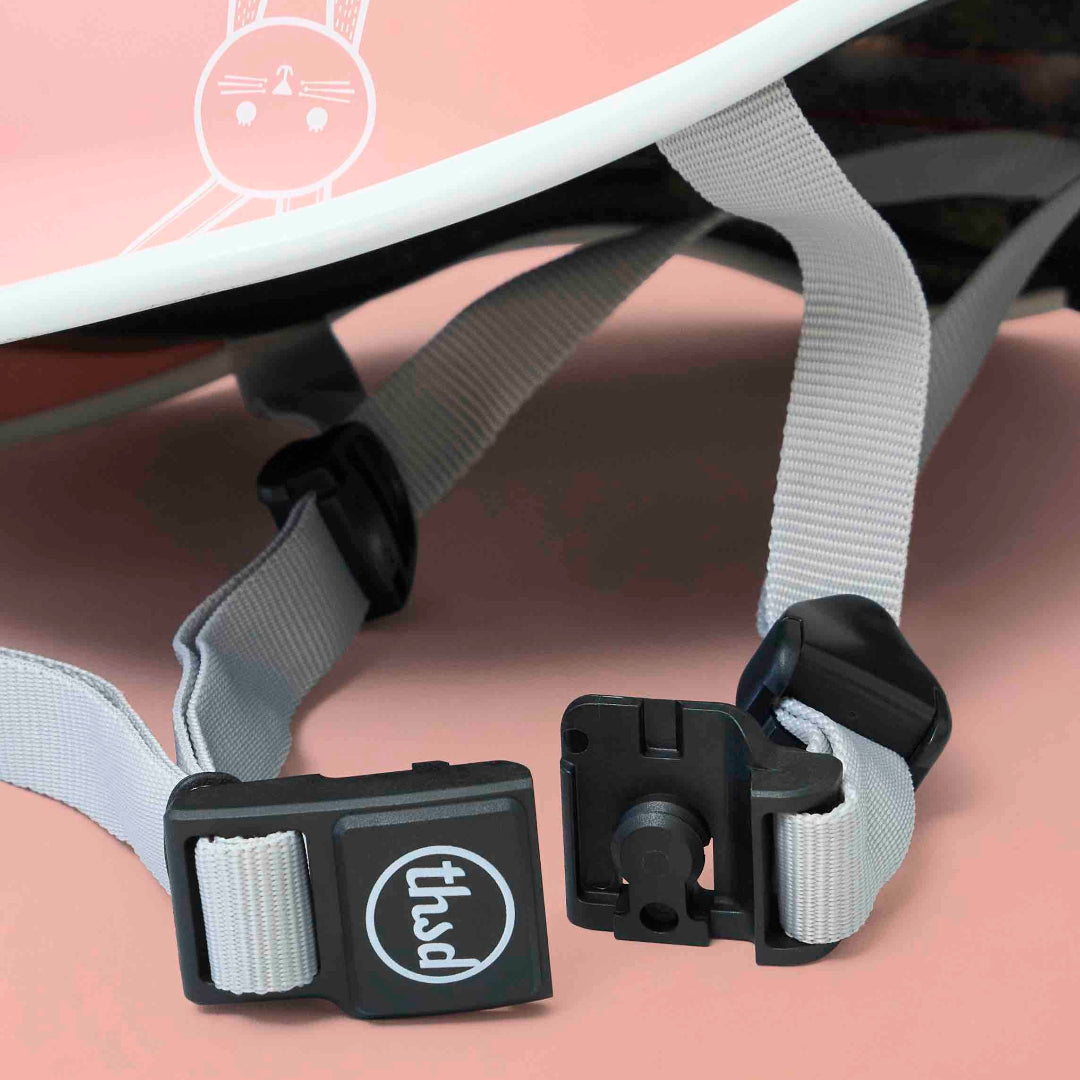 Close-up of a pink helmet with gray straps and black buckles, featuring the 'thsdl' brand logo.