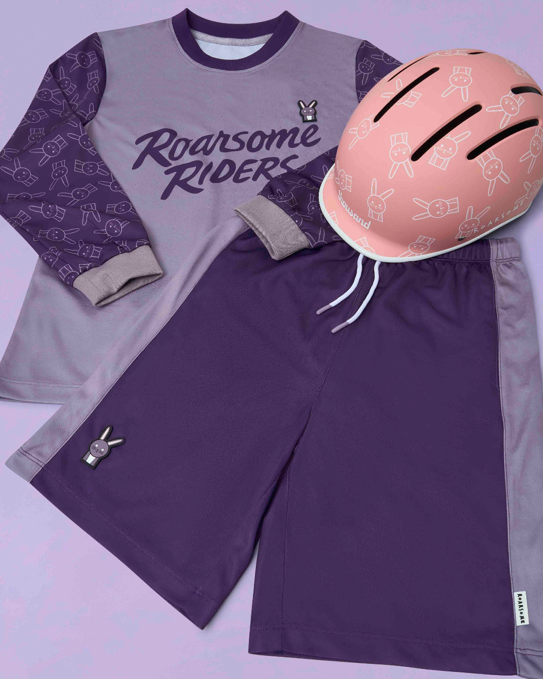 Purple and gray sports outfit with 'Roarsome Riders' text and a pink helmet on a light purple background