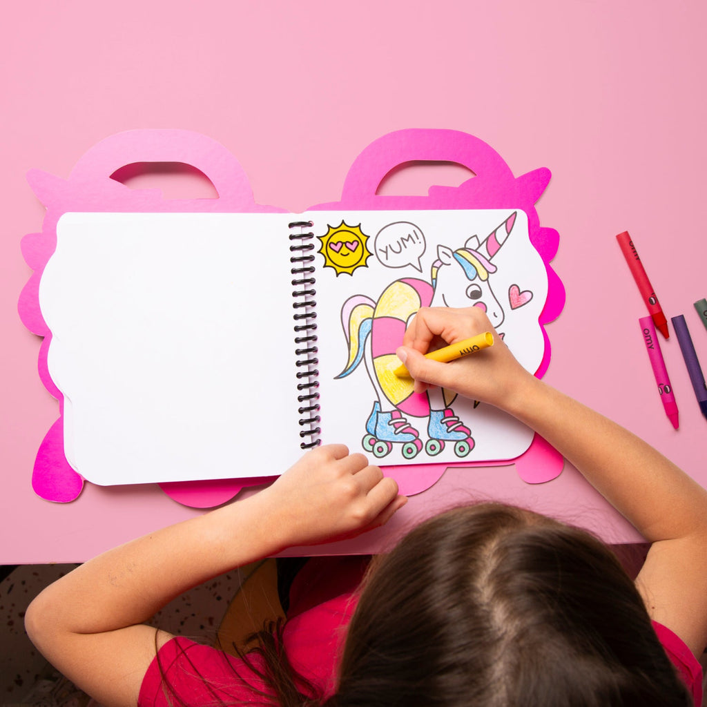 Child coloring a unicorn on a pink table with coloring book and markers.