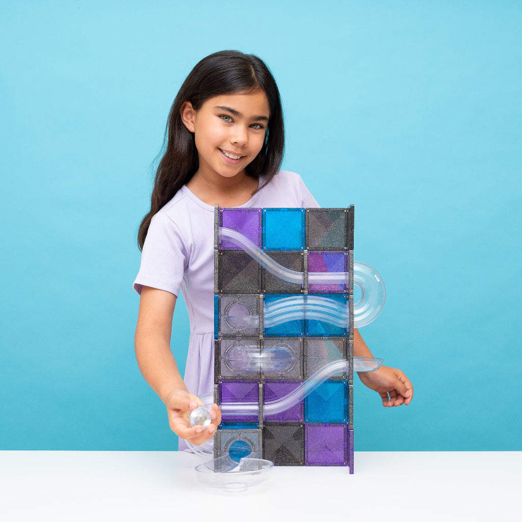 Girl holding a ball beside her CONNETIX Ball Run Galaxy build of black and purple glitter tiles