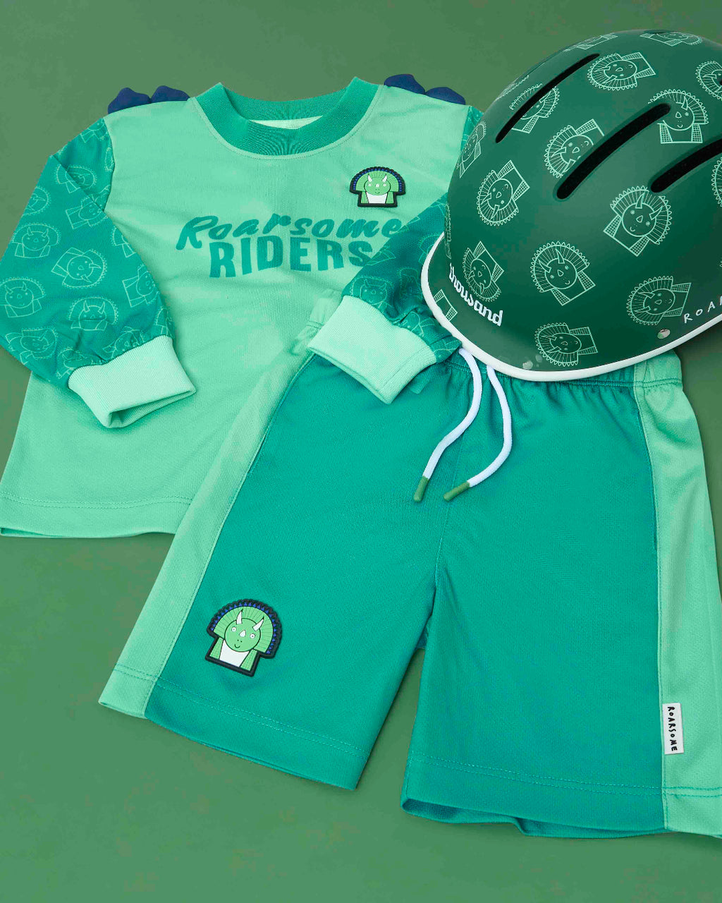 Children's green outfit with 'Roarsome Riders' text and helmet on a green background