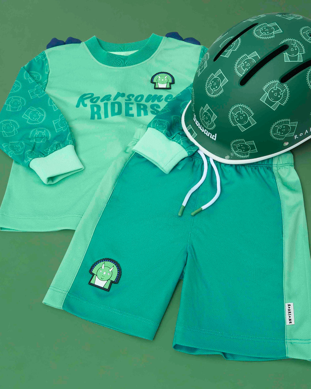 Children's green outfit with 'Roarsome Riders' text and helmet on a green background