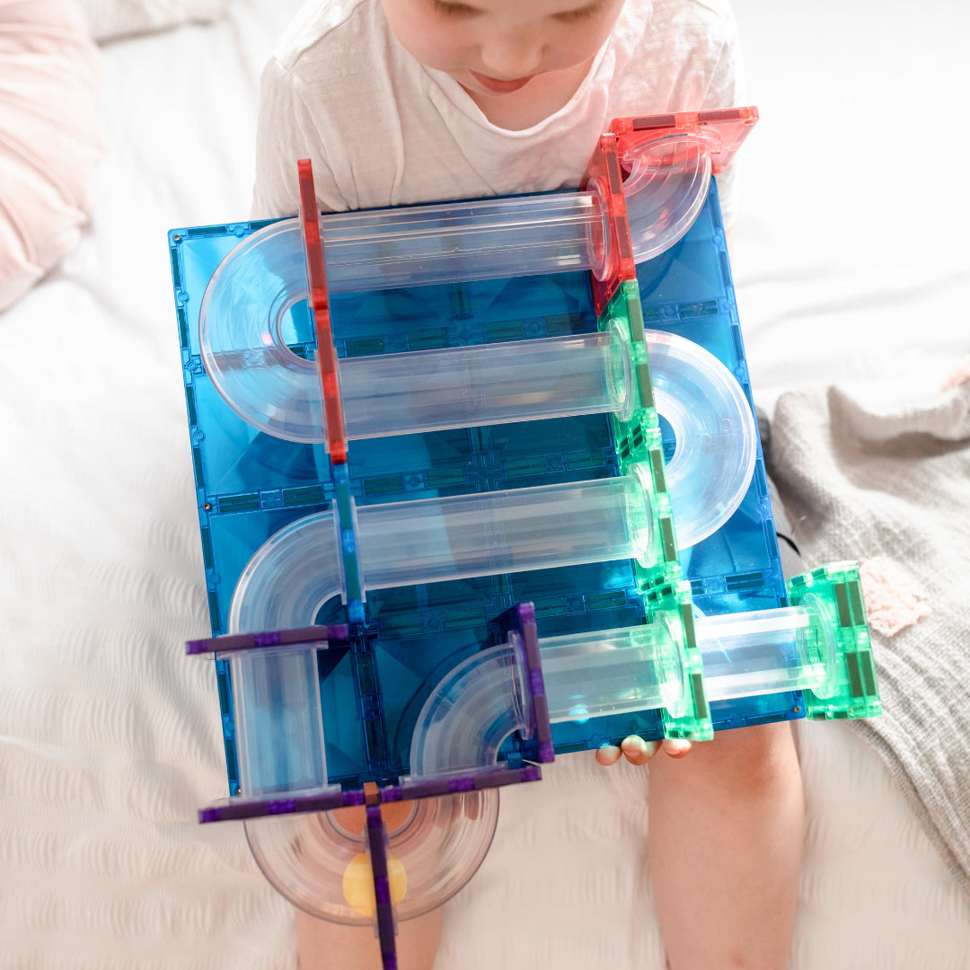 Child playing with a rainbow CONNETIX magnetic tile ball run on a white table