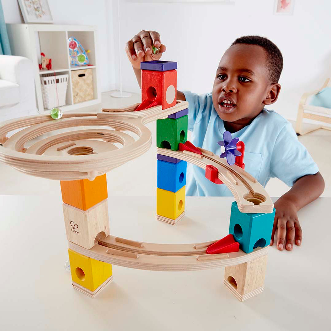 Child playing with a wooden marble run set in a bright living room.
