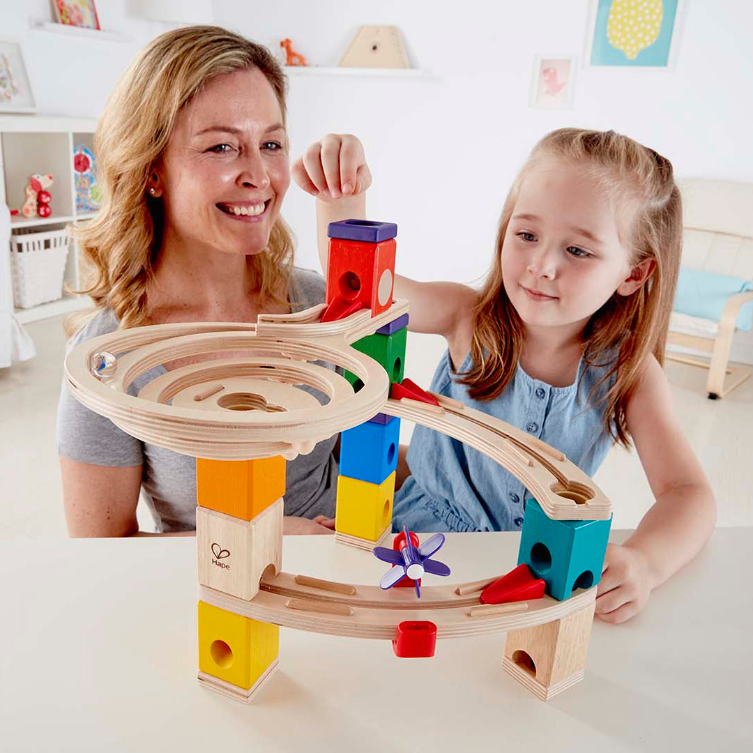 Woman and young girl playing with a colorful wooden toy in a bright living room.