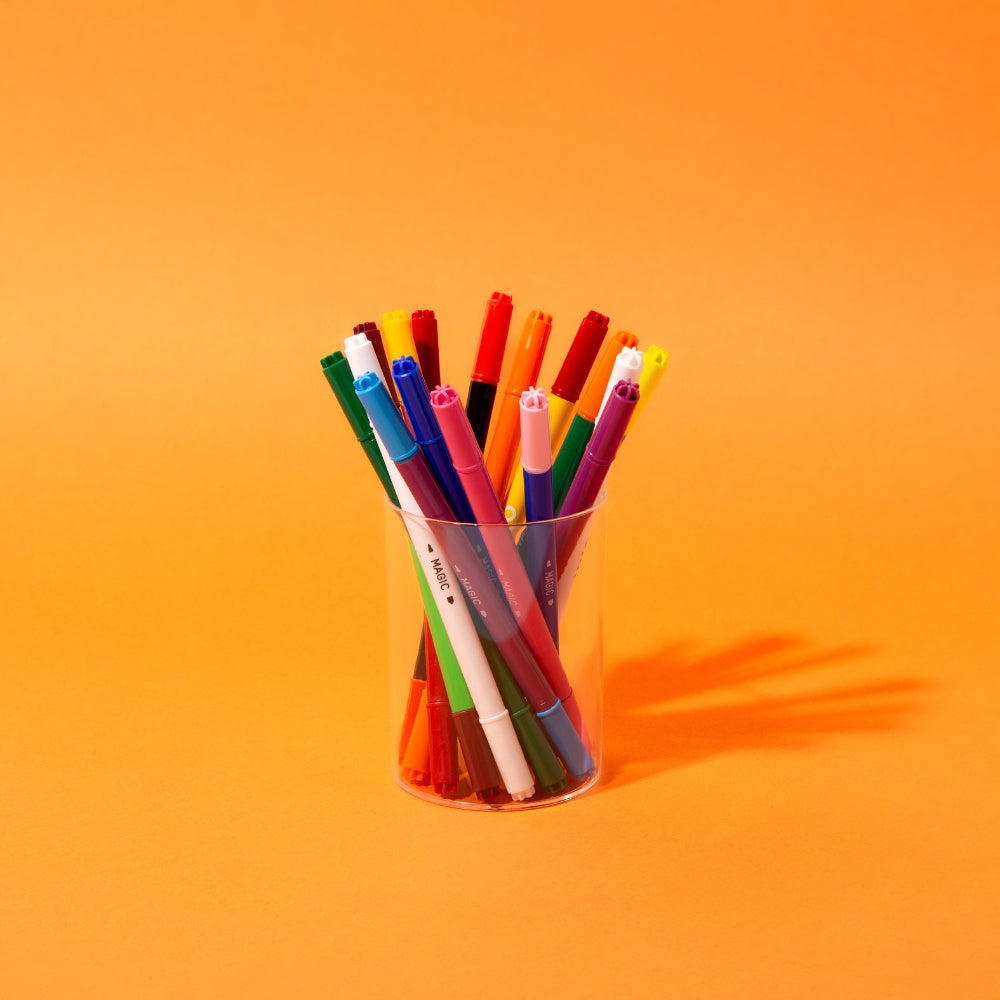 Colorful markers in a clear plastic cup on an orange background