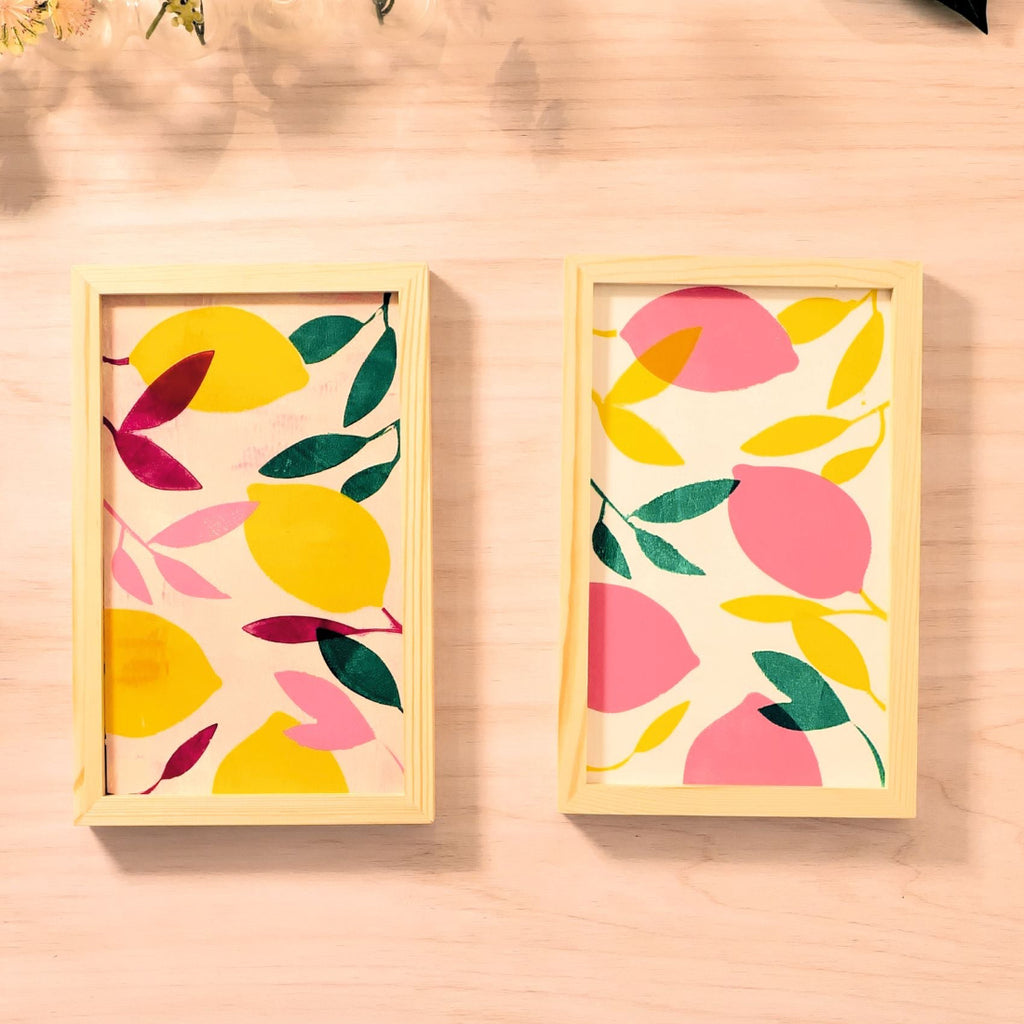 Two framed artworks with colorful lemon and leaf patterns on a wooden surface.