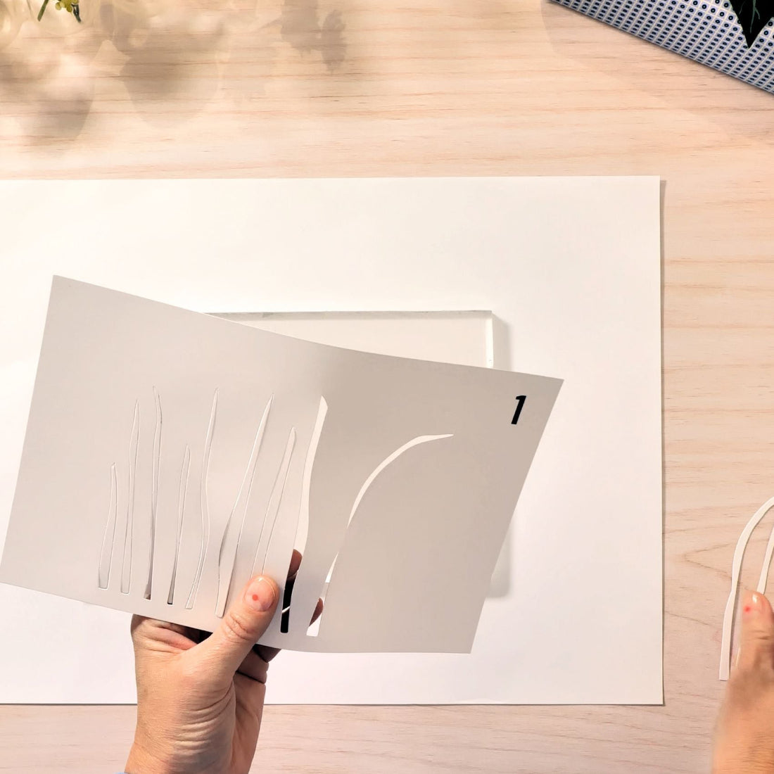 Person holding a white card with cut-out design on a wooden surface