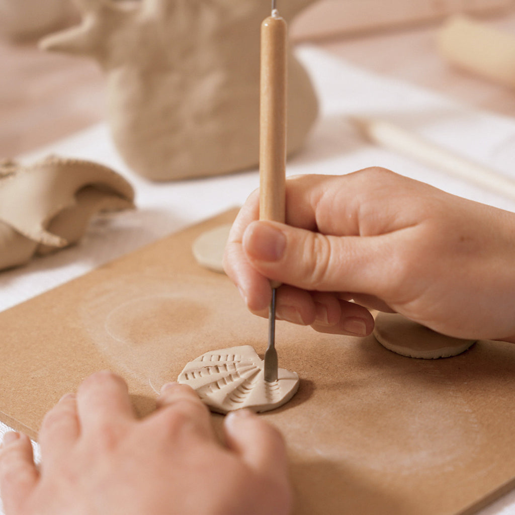 Person using a tool to shape clay on a wooden board