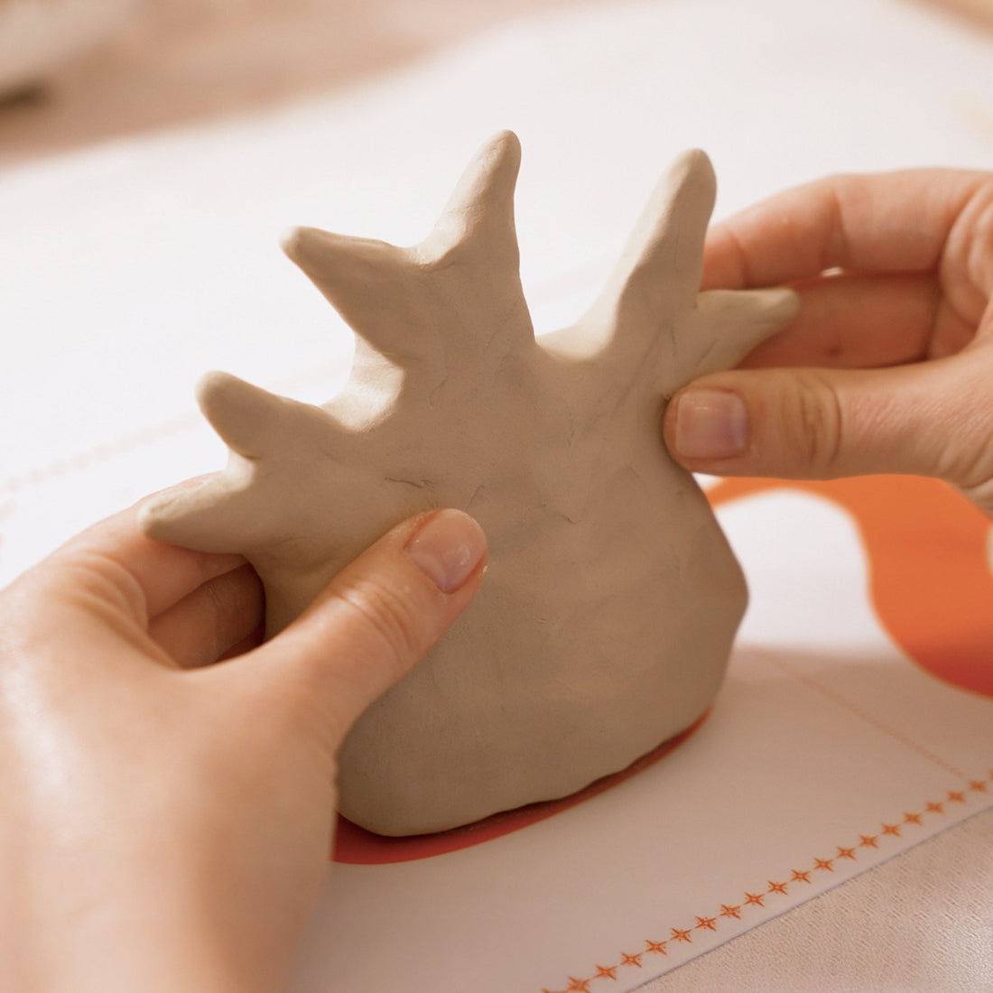 Person holding a small clay sculpture on a light surface.