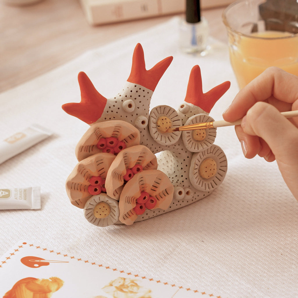 Person painting a ceramic object with a brush on a table.