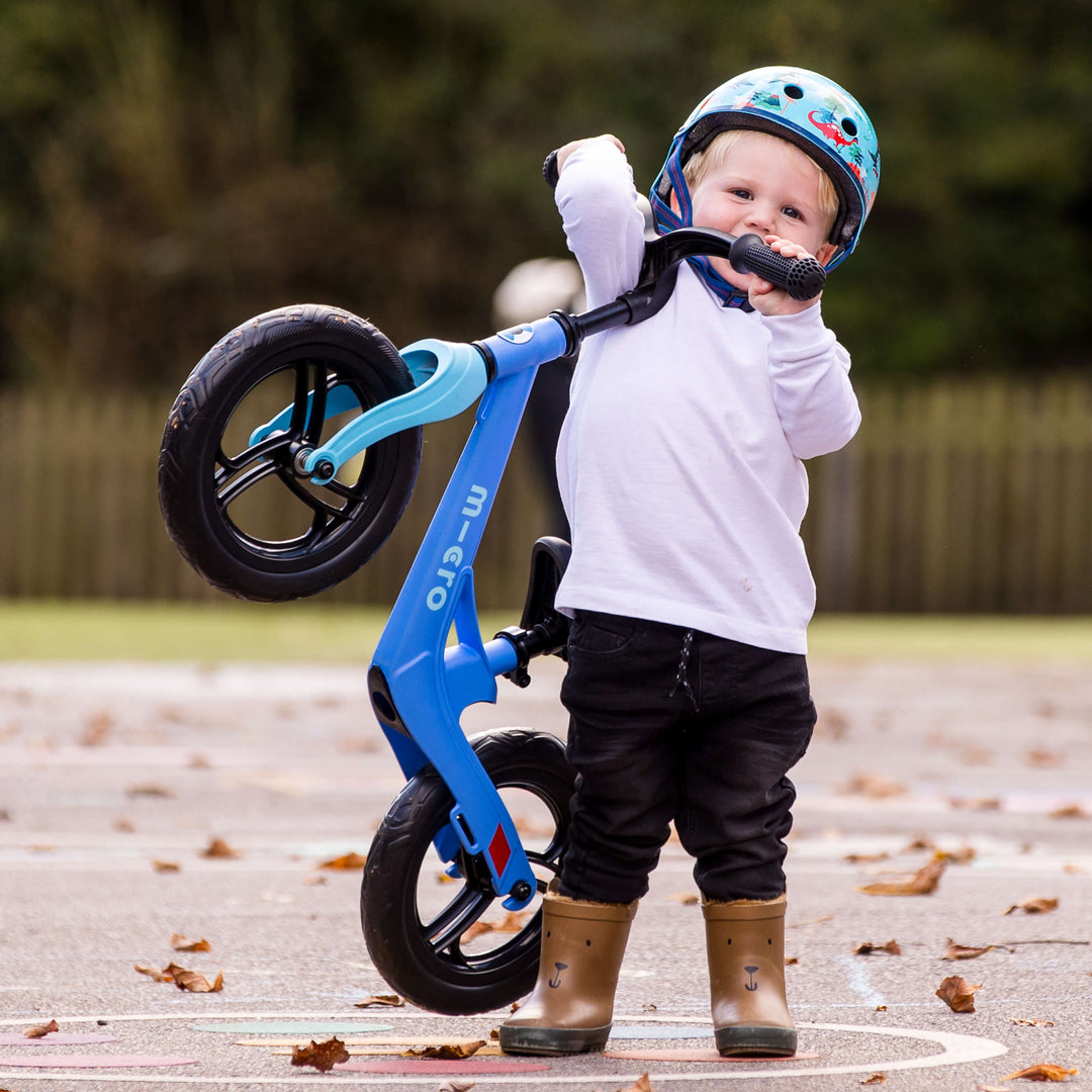 Toddler in a helmet lifting the front of the lightweight Micro Balance Bike Lite with one hand