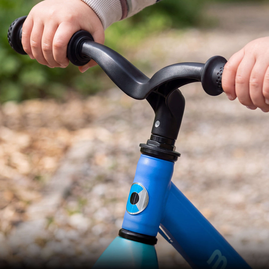 Close-up of a child's hands on the black handlebar grips of the blue Micro Balance Bike Lite