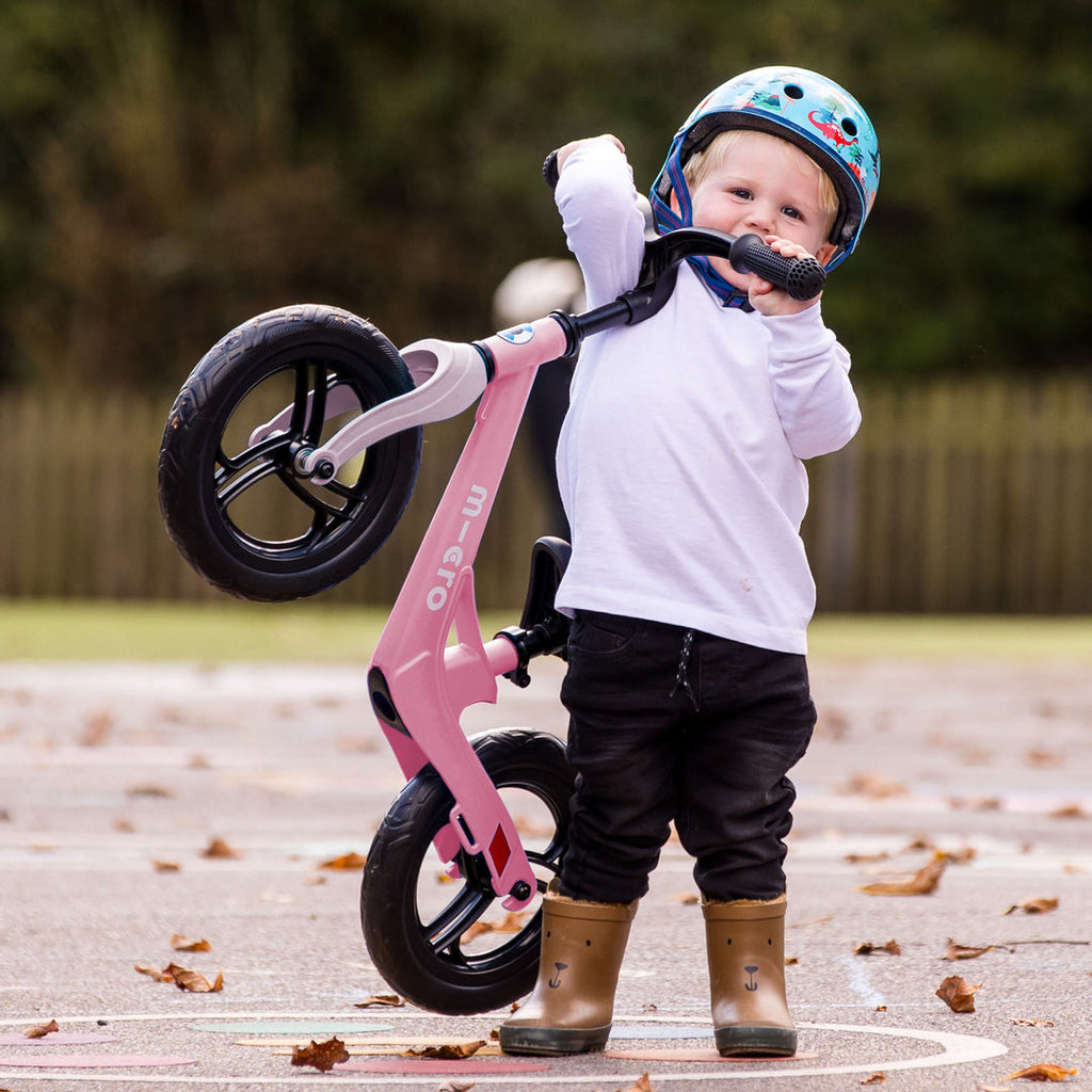 Toddler in a helmet lifting the front of the lightweight Micro Balance Bike Lite with one hand