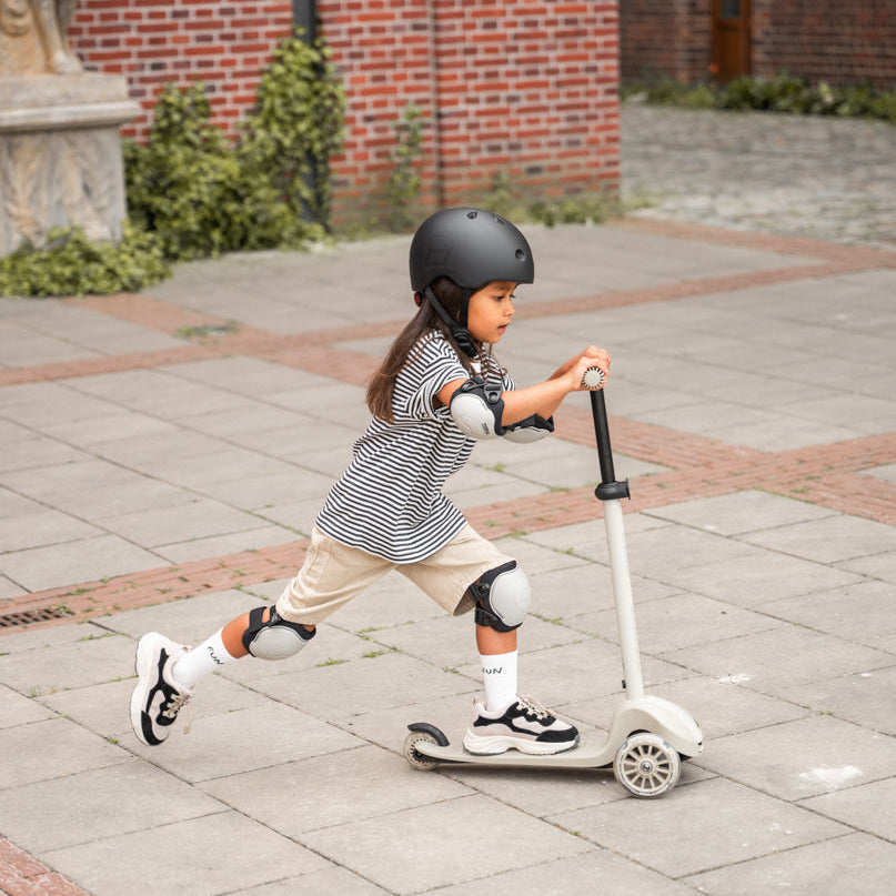 Child riding a scooter on a sidewalk with a brick building in the background