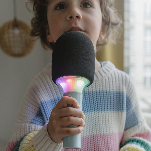 Child holding a microphone with colorful lights, wearing a striped sweater.