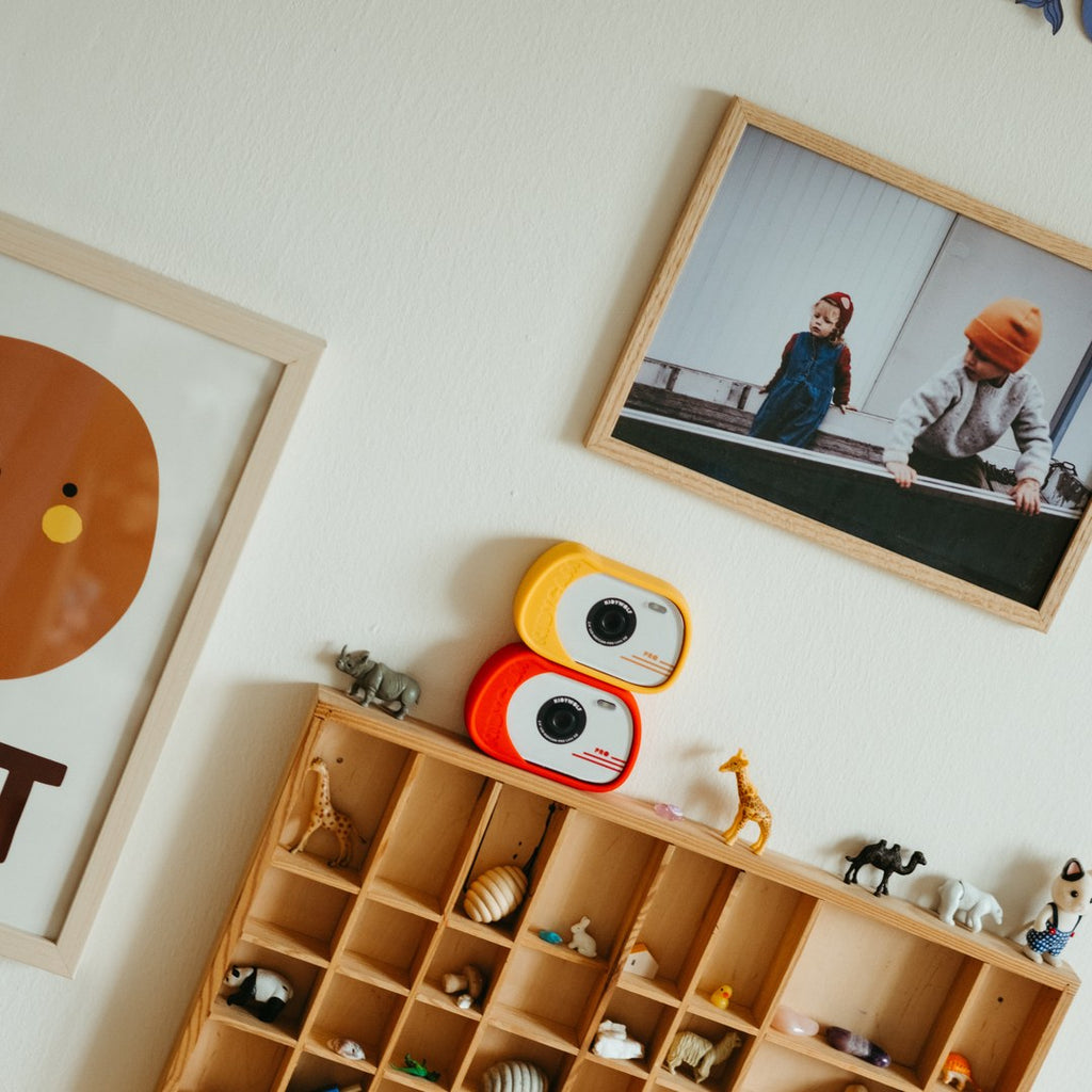 Orange and red KIDYCAM PRO cameras stacked on a wooden display shelf of toy animals in a child's bedroom