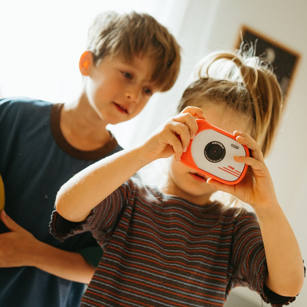 Girl taking a photo with a red KIDYCAM PRO while an older boy watches over her shoulder