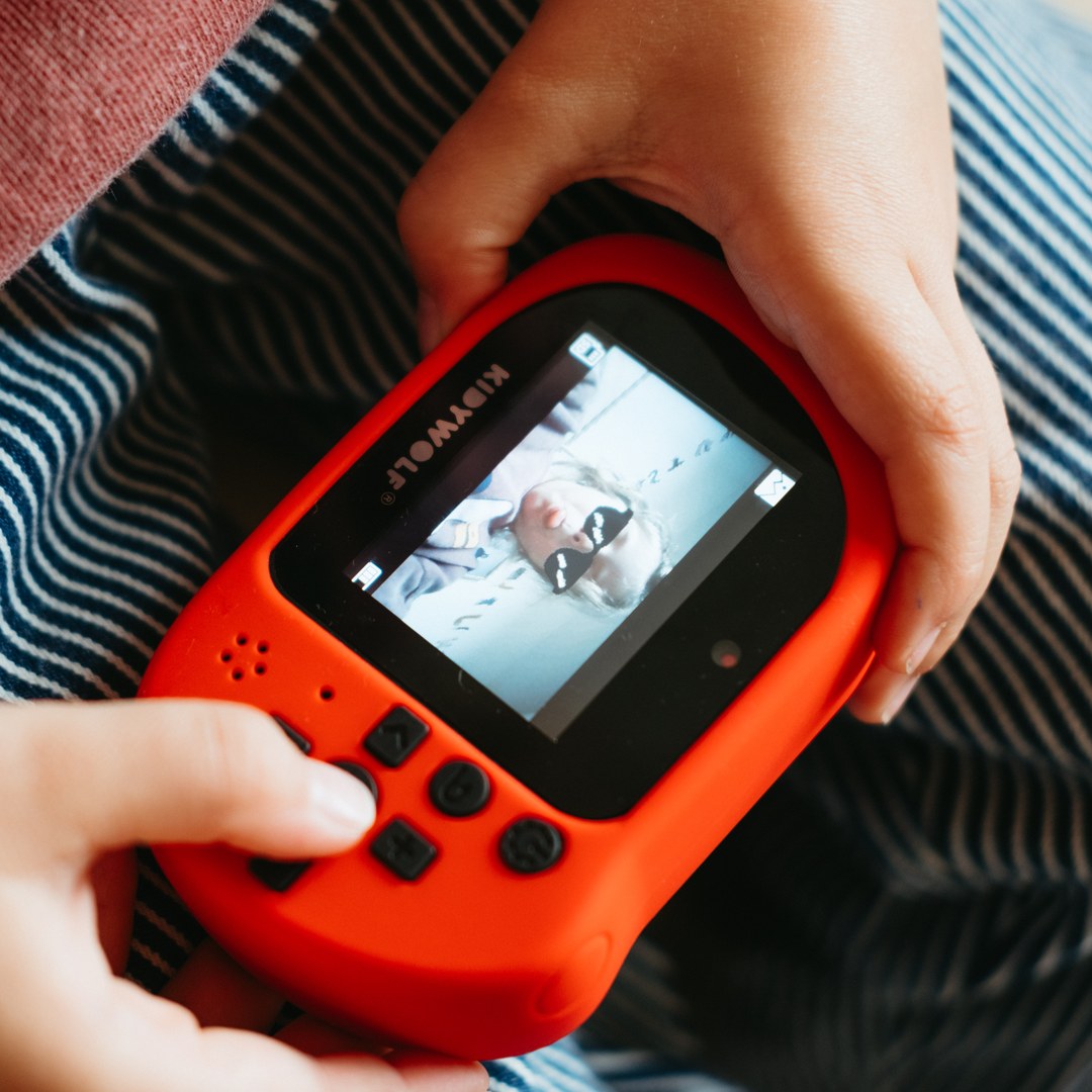 Close-up of a child's hands holding a red KIDYCAM PRO and looking at a photo on its screen