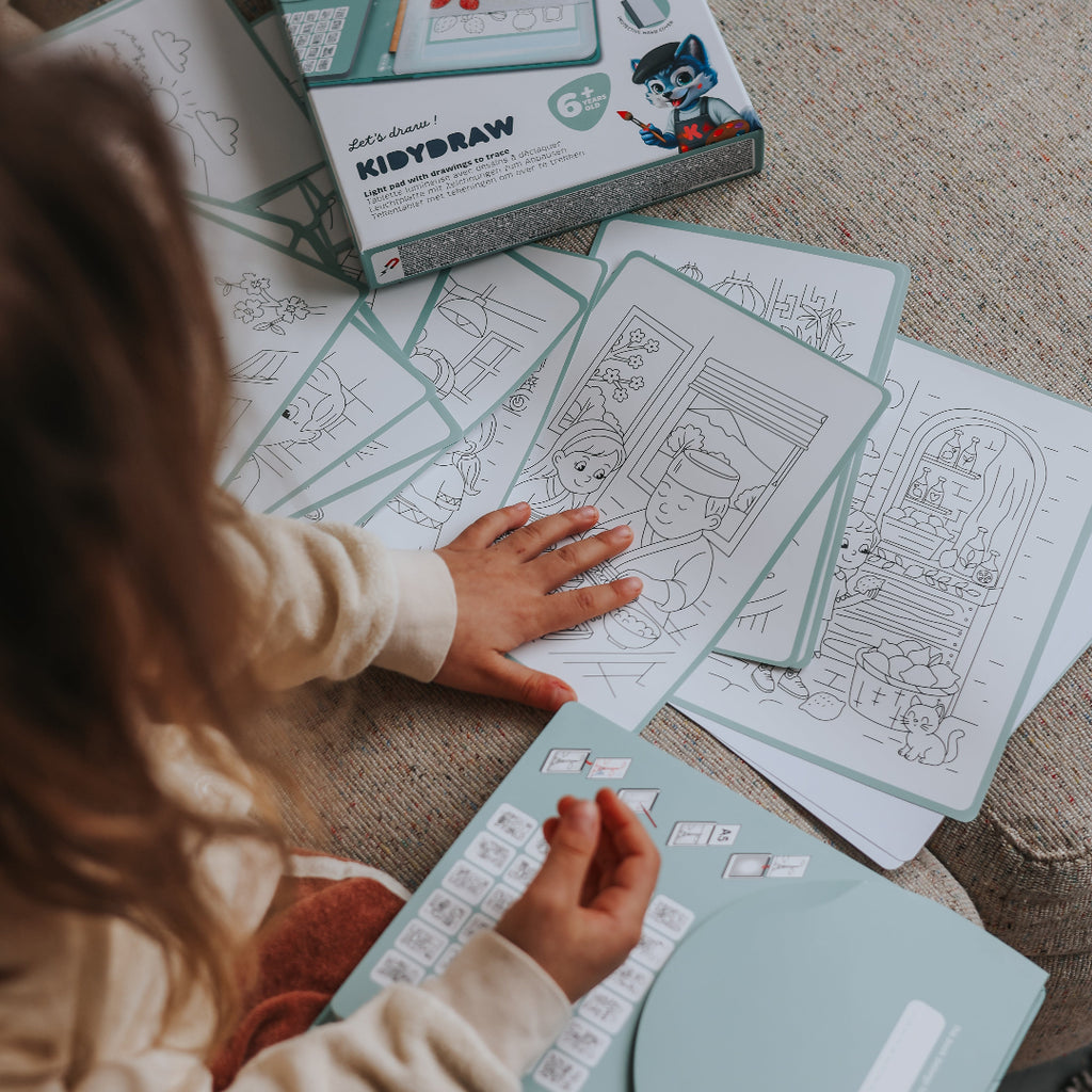 Child playing with coloring books and coloring sheets on a carpeted floor