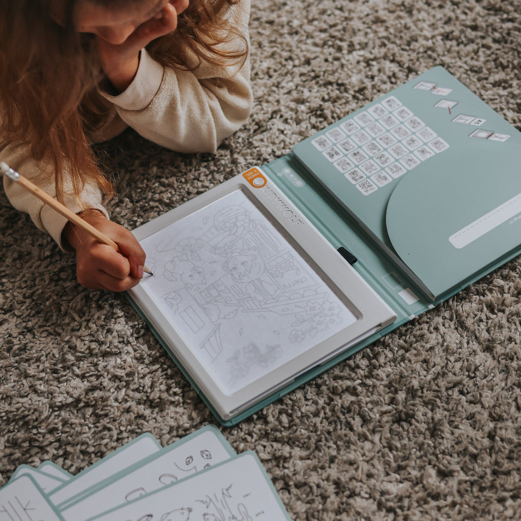 Child sitting on a carpeted floor with an open book and pages scattered around.