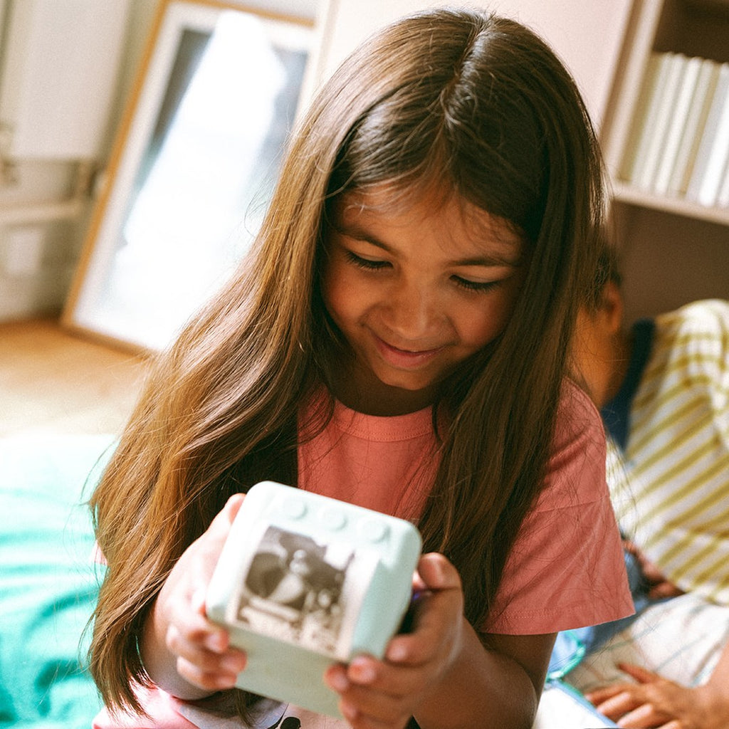 Smiling girl with long hair holding the green KIDYPRINTER AI with a black and white picture on its screen