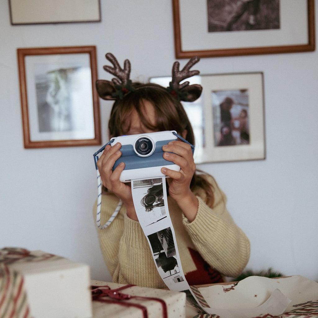 Child in a reindeer headband holding the blue K-PRINT up to their face while a strip of black and white prints comes out