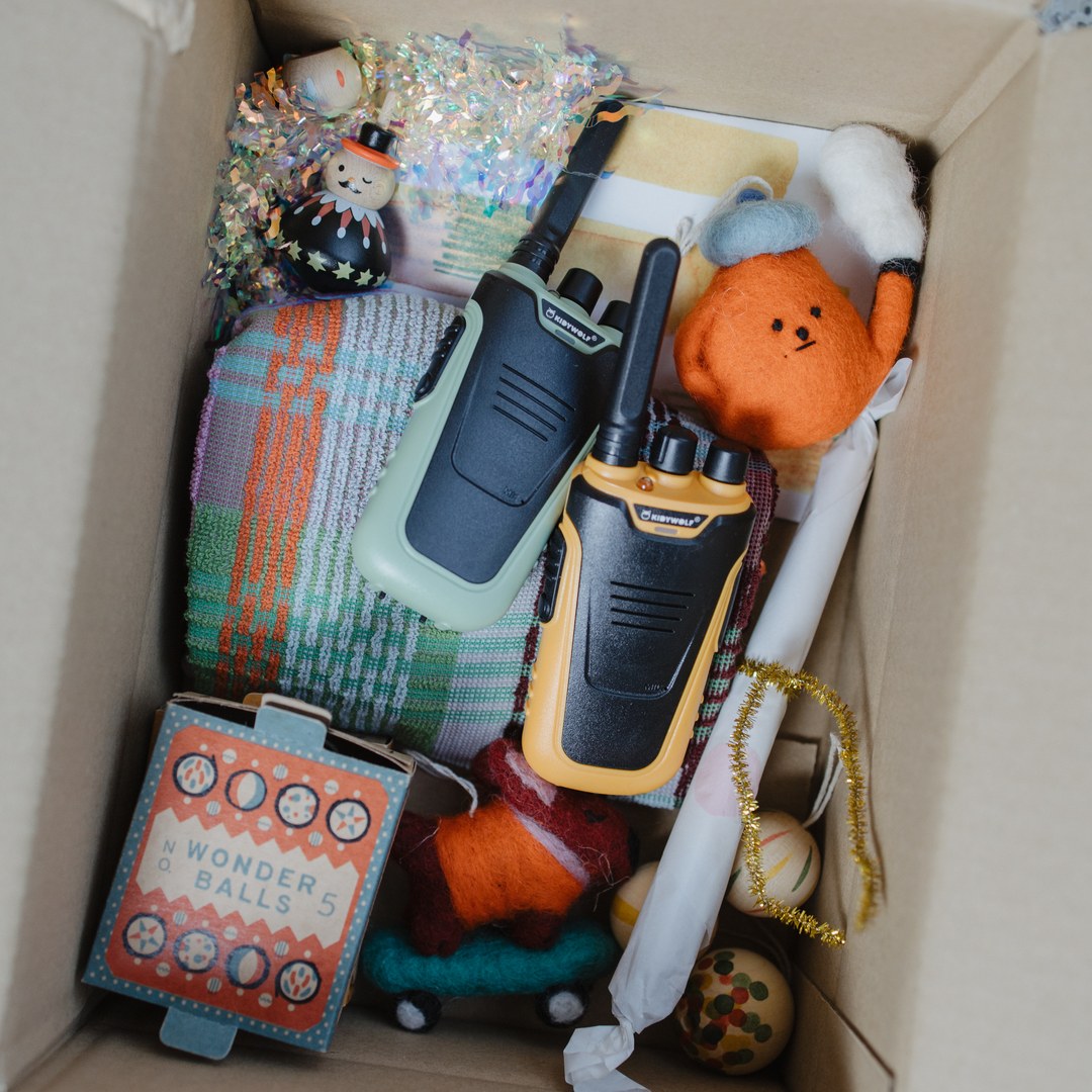Green and orange KIDYTALK walkie-talkies in a cardboard gift box with a blanket, felt toys and Christmas decorations