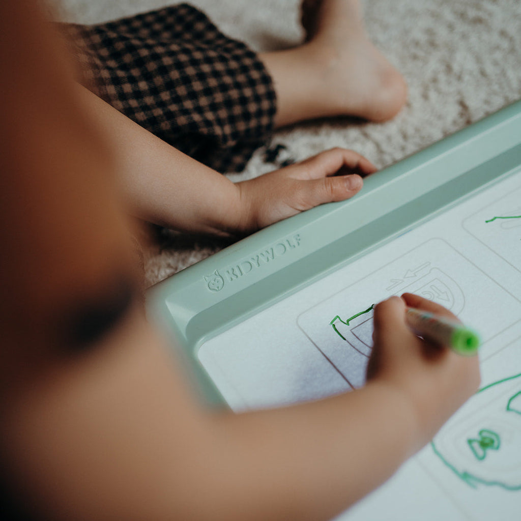 Child drawing on a tablet with feet visible on a carpeted floor.