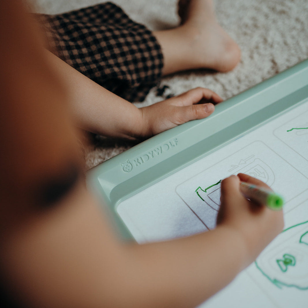 Child drawing on a tablet with feet visible on a carpeted floor.