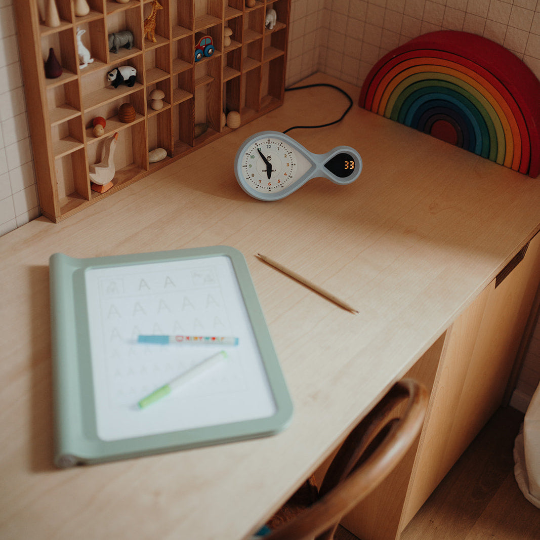 Children's desk with educational tools, clock, and rainbow decoration.