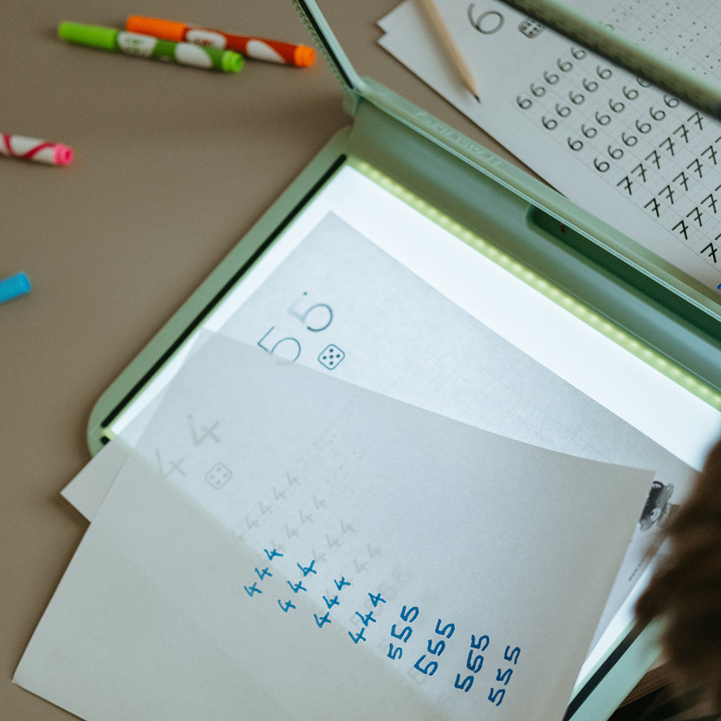 Child using a light-up board with numbers and writing tools on a table.