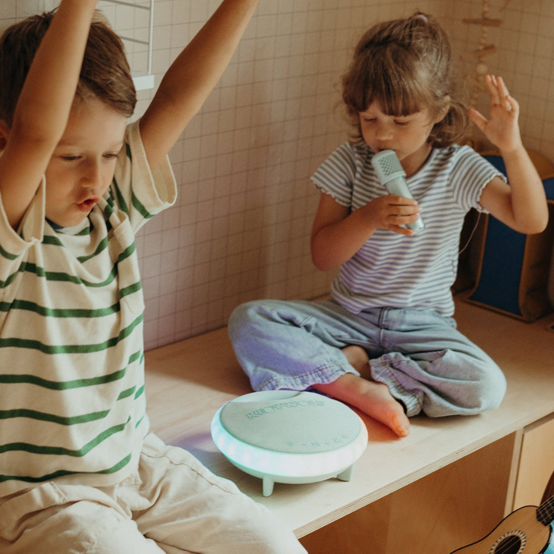 Two children playing with a karaoke toy on a wooden surface.