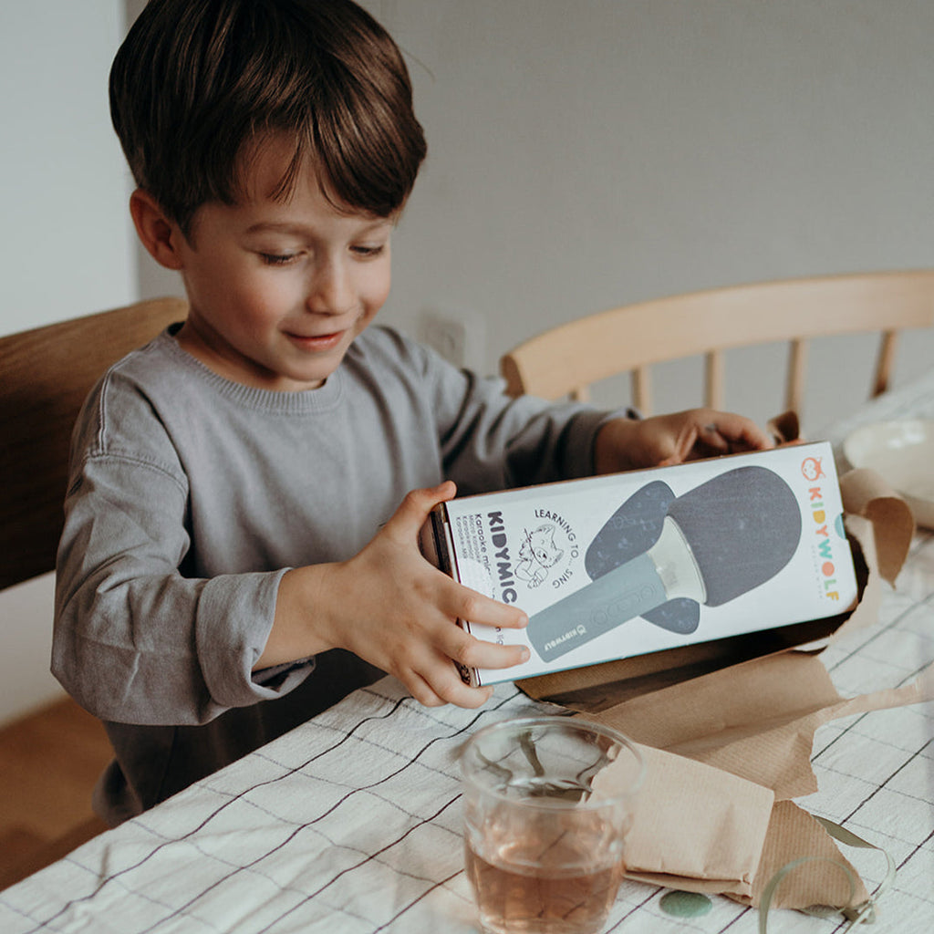 Child holding a book at a table with a cup and napkin