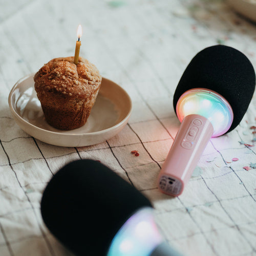 Two microphones with colorful lights near a cupcake with a lit candle on a patterned surface.
